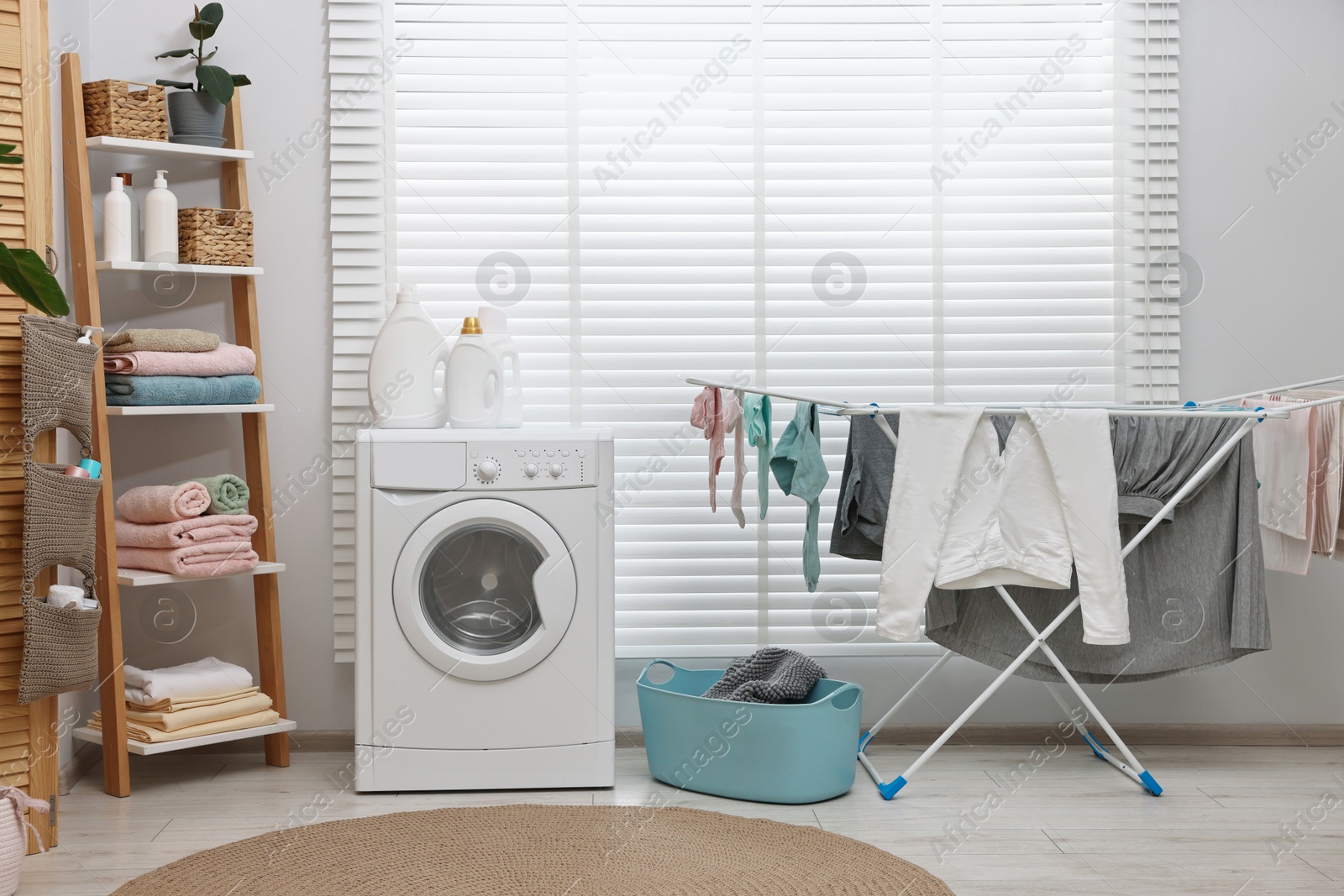 Photo of Washing machine, detergents, towels, basket and drying rack in laundry room