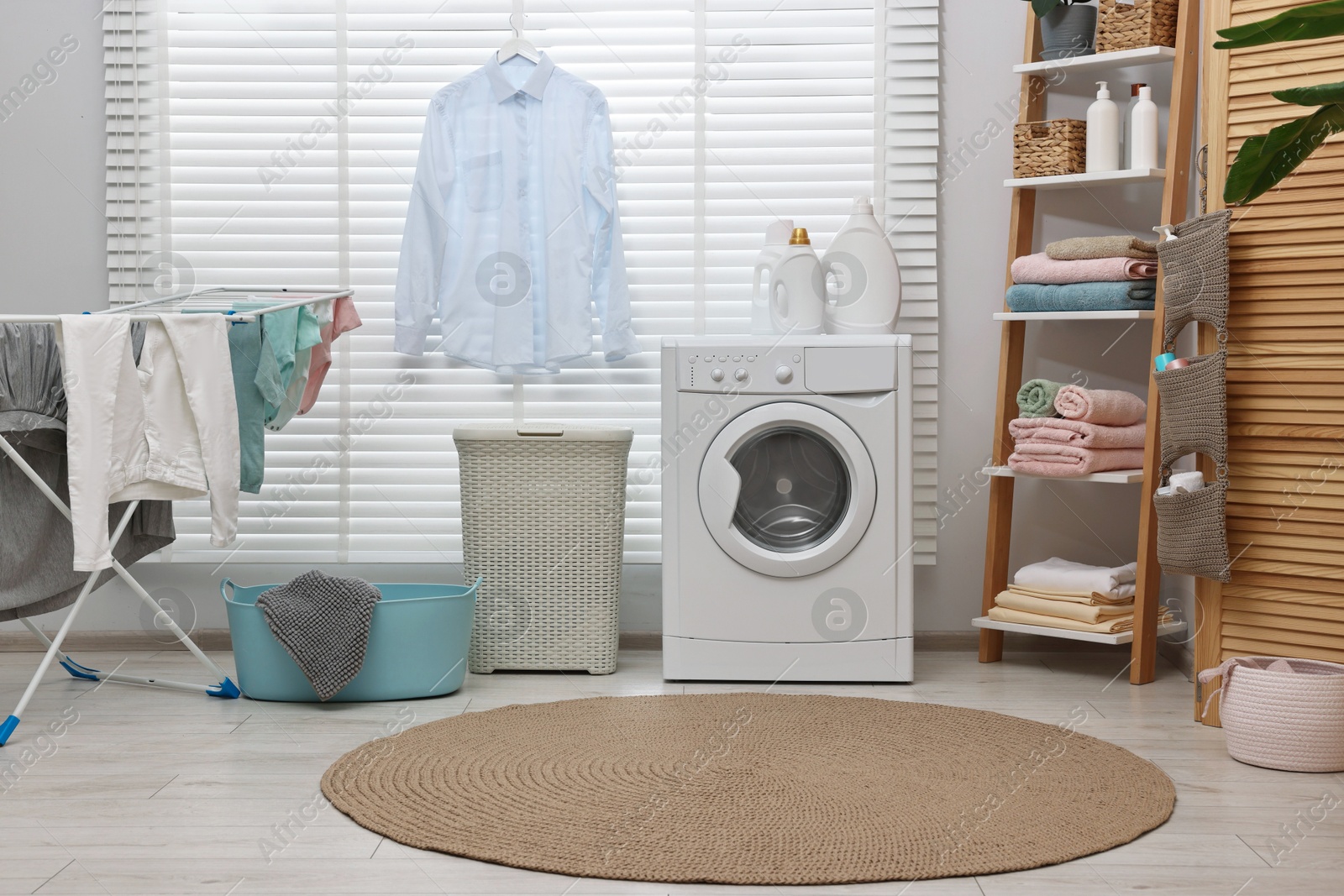 Photo of Washing machine, detergents, towels, baskets and drying rack in laundry room