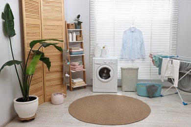 Photo of Washing machine, detergents, towels, baskets and drying rack in laundry room