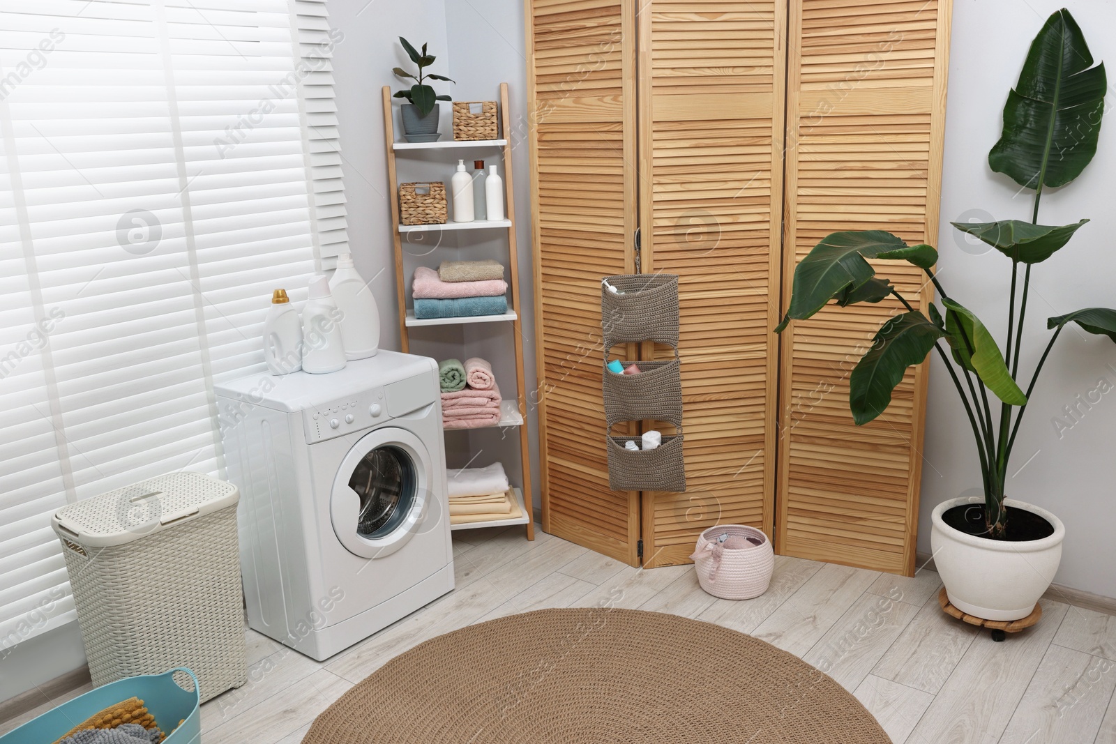 Photo of Washing machine, folding screen, detergents, towels and basket in laundry room