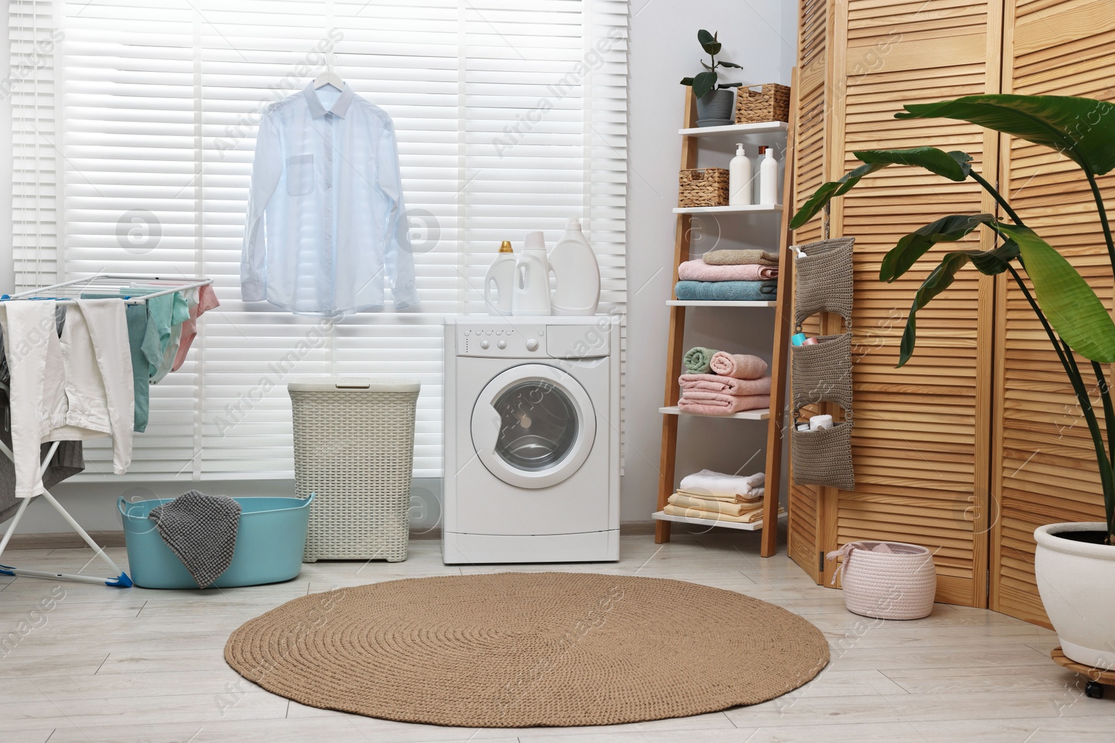 Photo of Washing machine, detergents, towels, baskets and drying rack in laundry room