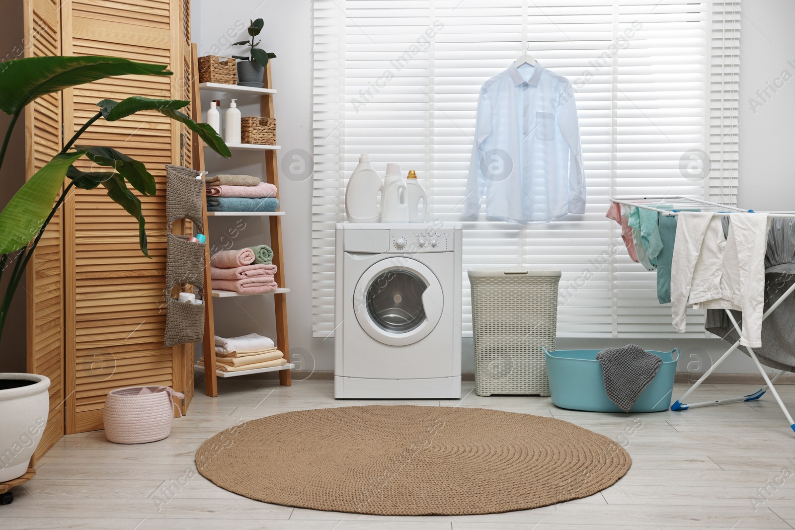 Photo of Washing machine, detergents, towels, baskets and drying rack in laundry room