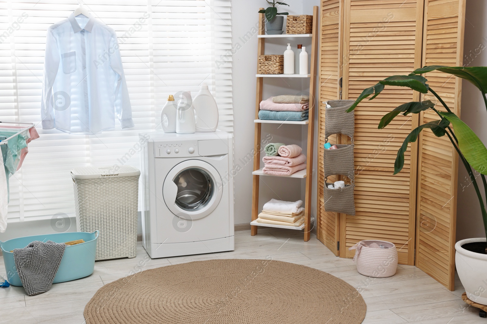 Photo of Washing machine, detergents, towels, baskets and folding screen in laundry room