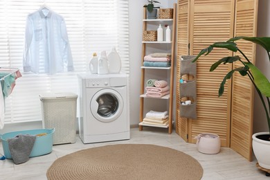 Photo of Washing machine, detergents, towels, baskets and folding screen in laundry room