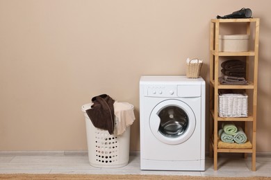 Photo of Washing machine, basket and shelving unit near beige wall indoors. Space for text