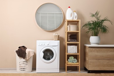 Photo of Stylish laundry room interior with washing machine, furniture, detergents and houseplant