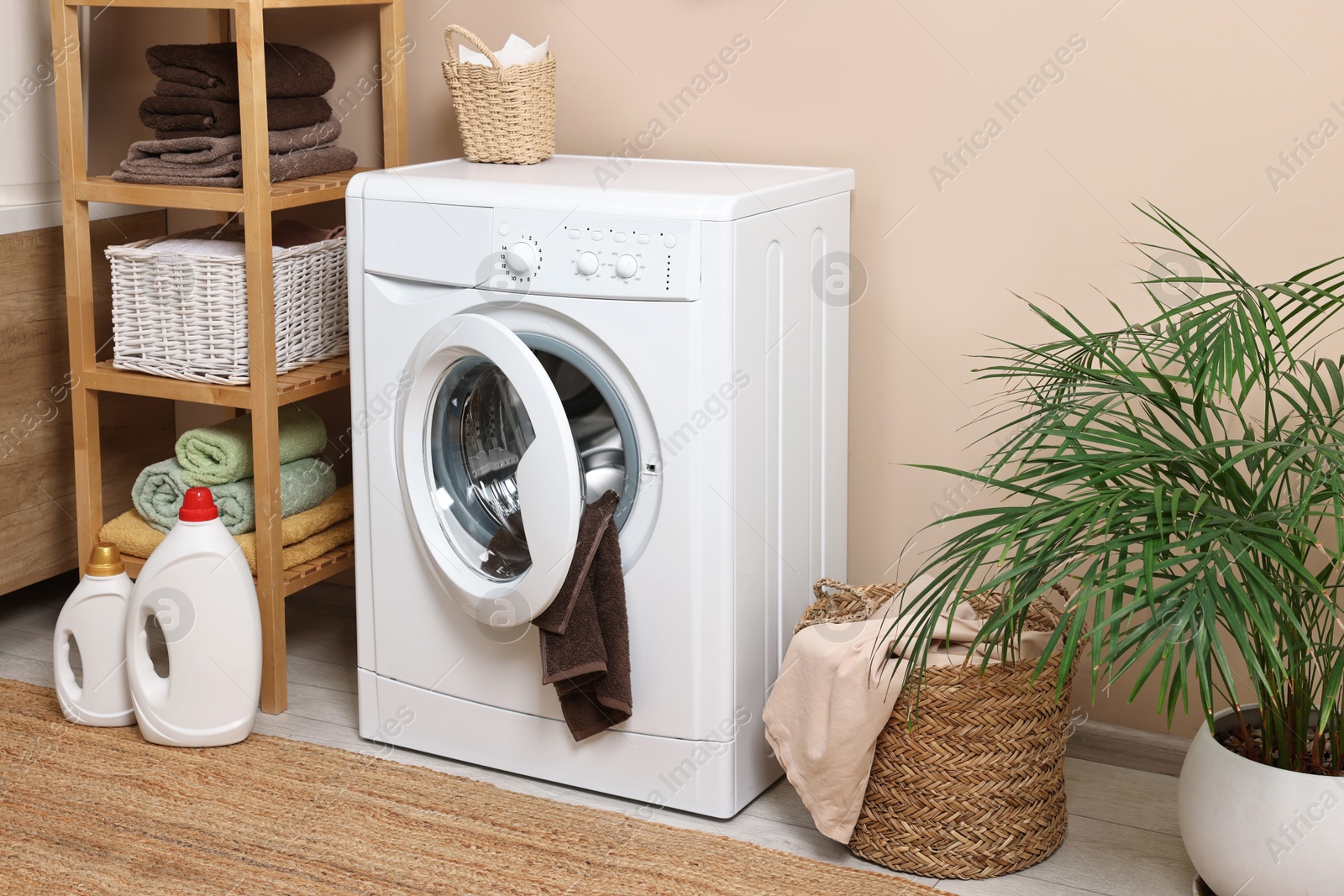 Photo of Stylish laundry room interior with washing machine, furniture, detergents and houseplant