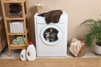 Photo of Stylish laundry room interior with washing machine, furniture, detergents and houseplant