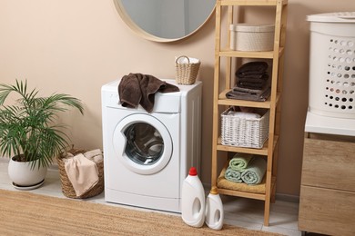 Stylish laundry room interior with washing machine, furniture and houseplant