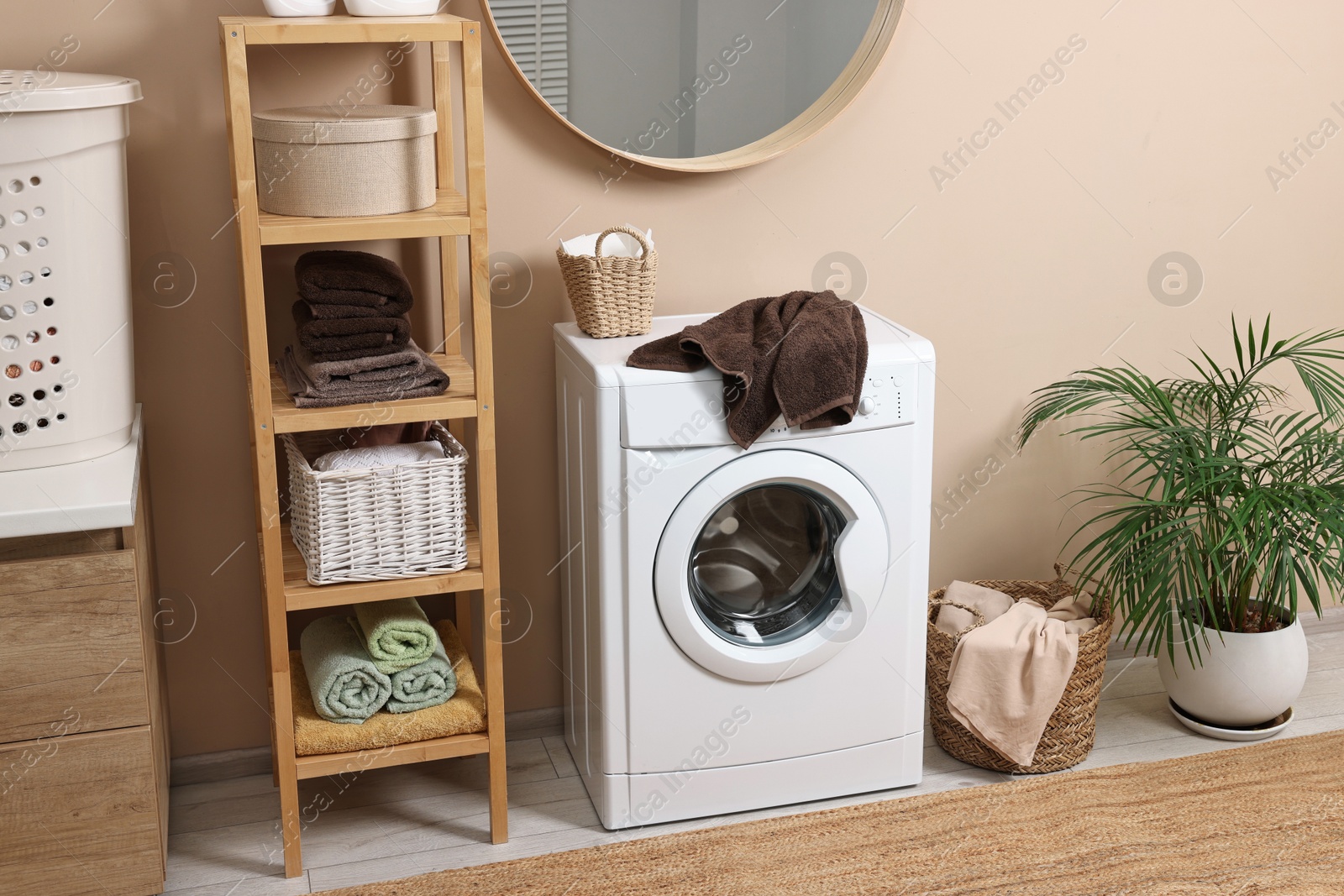 Photo of Stylish laundry room interior with washing machine, furniture and houseplant