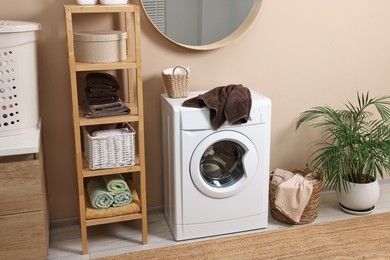 Stylish laundry room interior with washing machine, furniture and houseplant