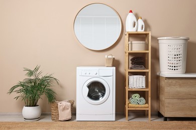 Stylish laundry room interior with washing machine, furniture and houseplant