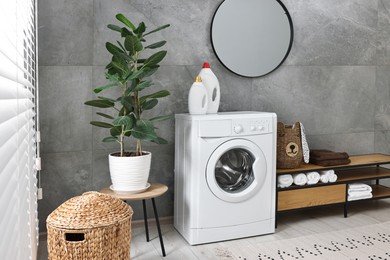 Photo of Washing machine, detergents, houseplant, baskets and storage cabinet in laundry room