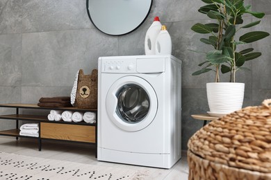 Photo of Washing machine, detergents, houseplant, baskets and storage cabinet in laundry room