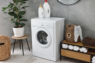 Photo of Washing machine, detergents, houseplant, baskets and storage cabinet in laundry room