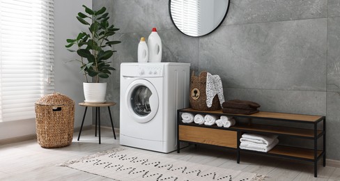 Photo of Washing machine, detergents, houseplant, baskets and storage cabinet in laundry room