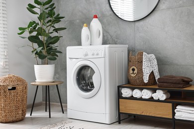 Photo of Washing machine, detergents, houseplant, baskets and storage cabinet in laundry room