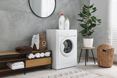 Photo of Washing machine, detergents, houseplant, baskets and storage cabinet in laundry room