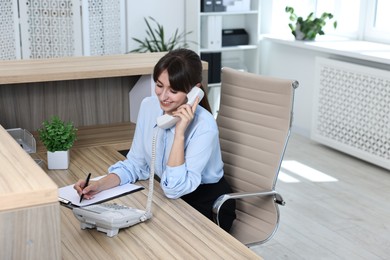 Photo of Professional receptionist talking on phone in office