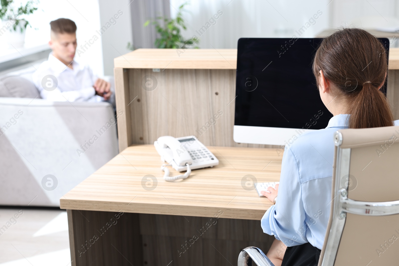 Photo of Professional receptionist working at wooden desk in office, back view