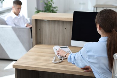 Photo of Professional receptionist working at wooden desk in office, back view