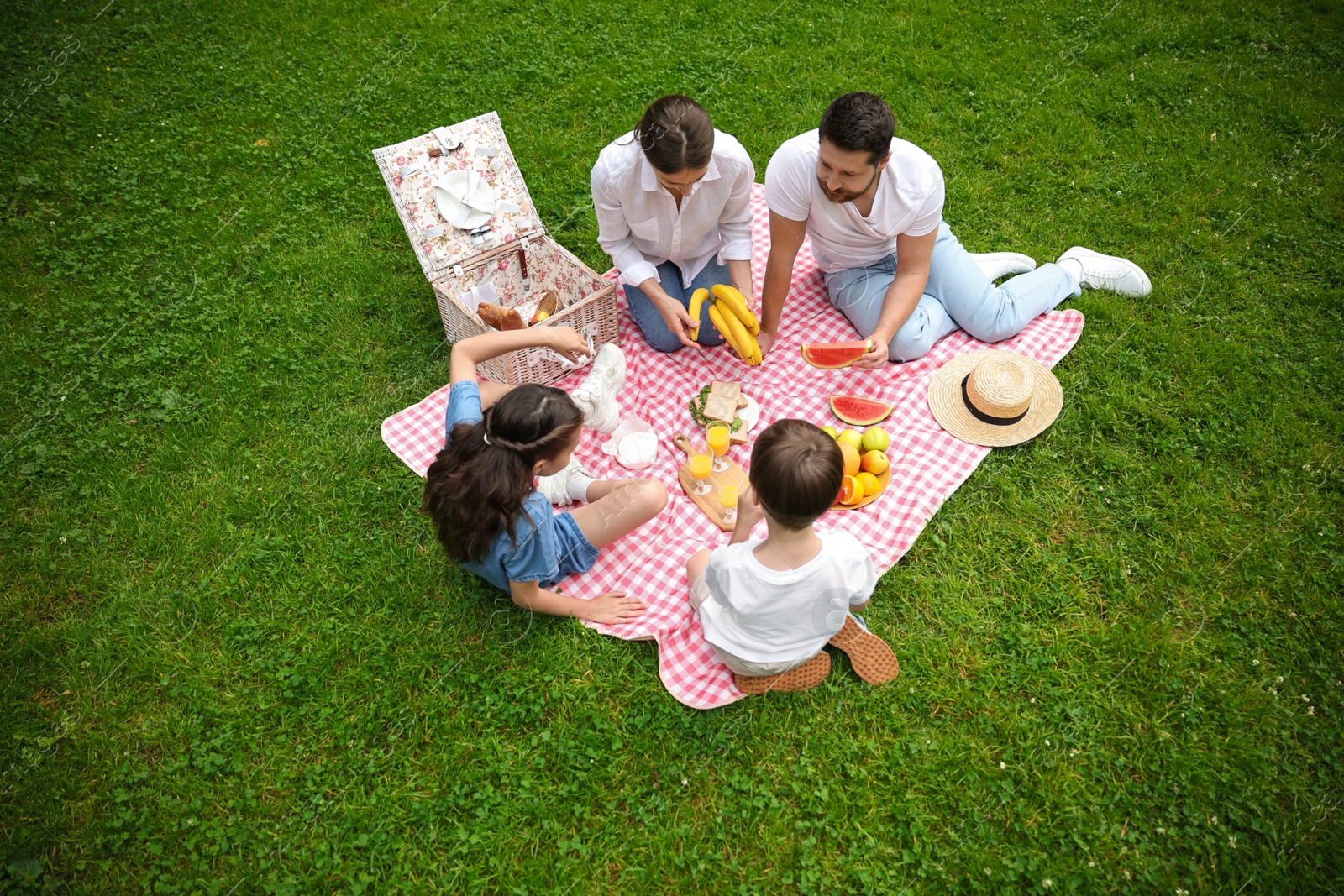 Photo of Family picnic. Parents and their children eating on green grass outdoors, above view