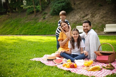 Photo of Family picnic. Happy parents and their children spending time together on green grass outdoors. Space for text