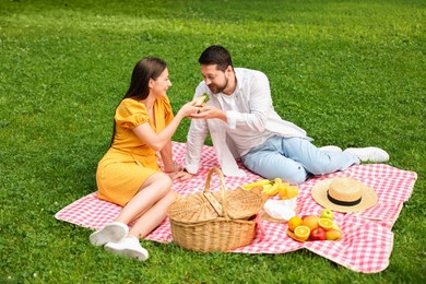 Photo of Romantic picnic. Woman feeding her boyfriend on blanket outdoors