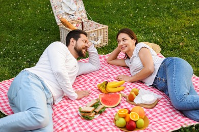 Photo of Happy couple having picnic on green grass outdoors