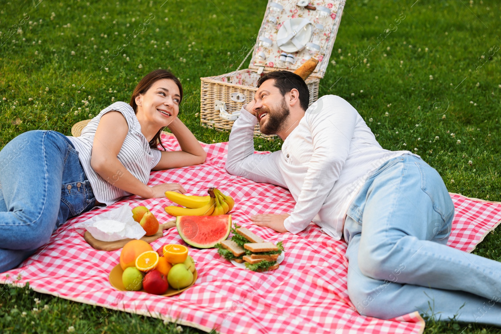 Photo of Happy couple having picnic on green grass outdoors