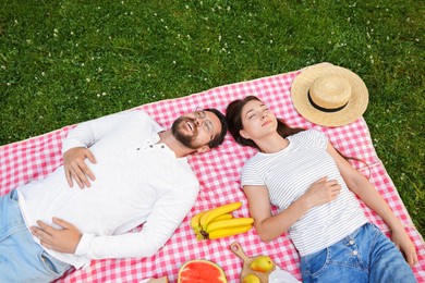 Photo of Romantic picnic. Happy couple relaxing together on green grass outdoors, top view