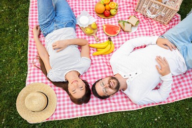 Photo of Romantic picnic. Happy couple relaxing together on green grass outdoors, above view