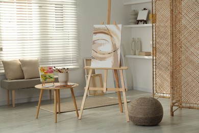 Photo of Folding screen and easels with beautiful abstract paintings in room