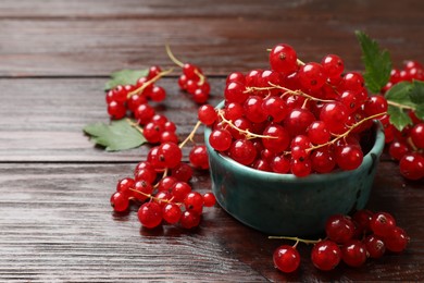 Photo of Fresh red currants and green leaves on wooden table, closeup