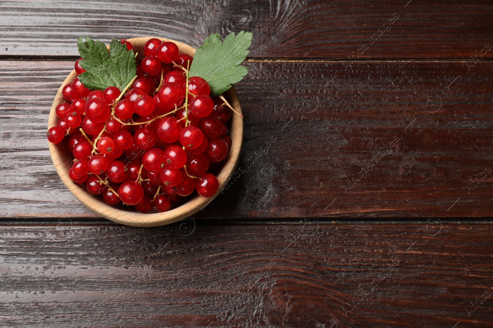 Photo of Fresh red currants in bowl on wooden table, top view. Space for text