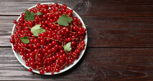 Photo of Fresh red currants and leaves on wooden table, top view. Space for text