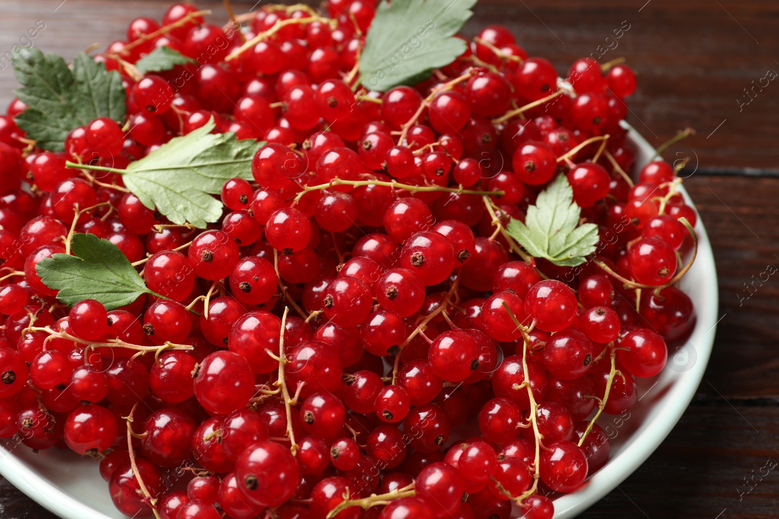 Photo of Fresh red currants and leaves on wooden table, closeup