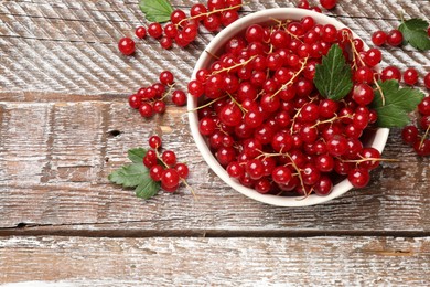 Photo of Fresh red currants in bowl and green leaves on wooden table, top view. Space for text