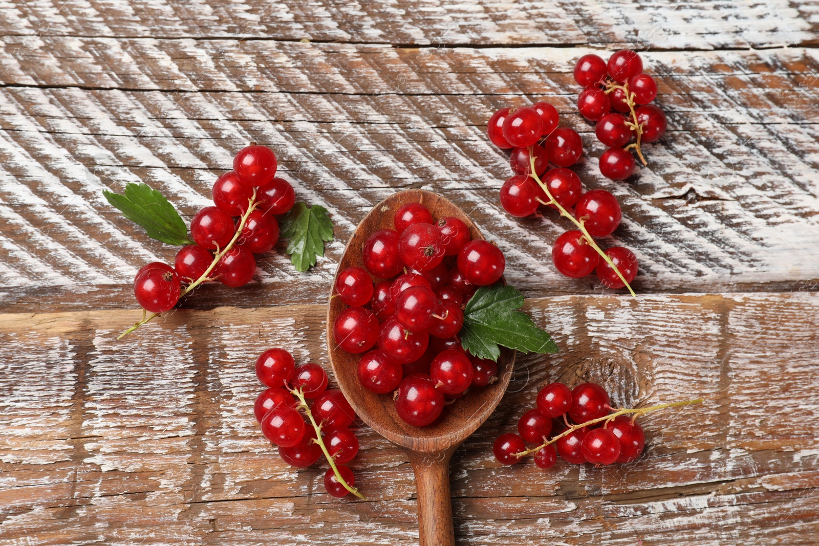 Photo of Fresh red currants and green leaves on wooden table, top view