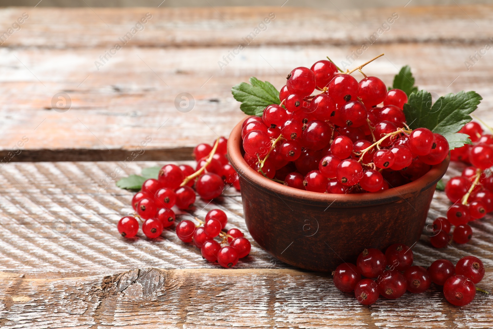 Photo of Fresh red currants in bowl on wooden table, closeup. Space for text