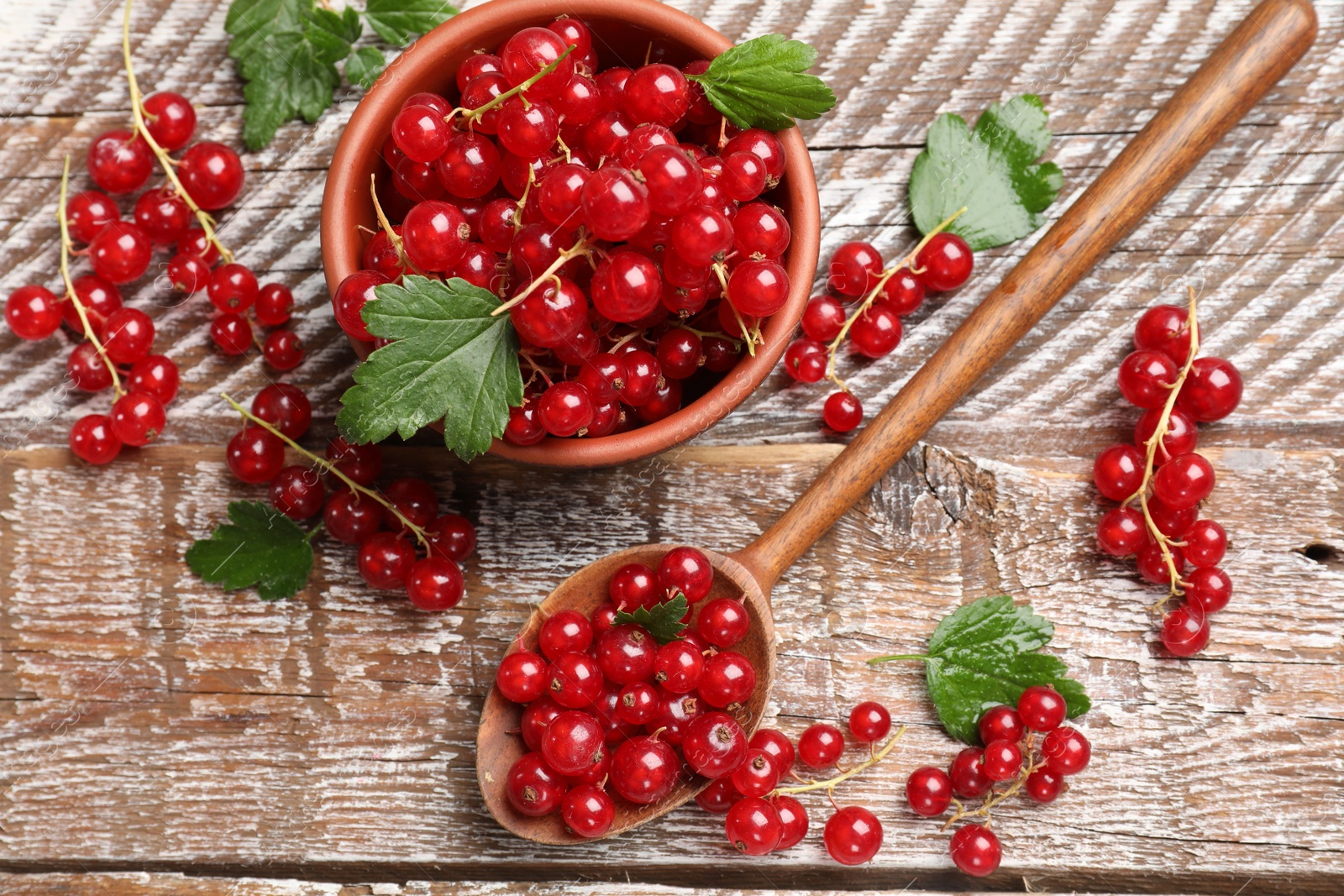 Photo of Fresh red currants and green leaves on wooden table, flat lay