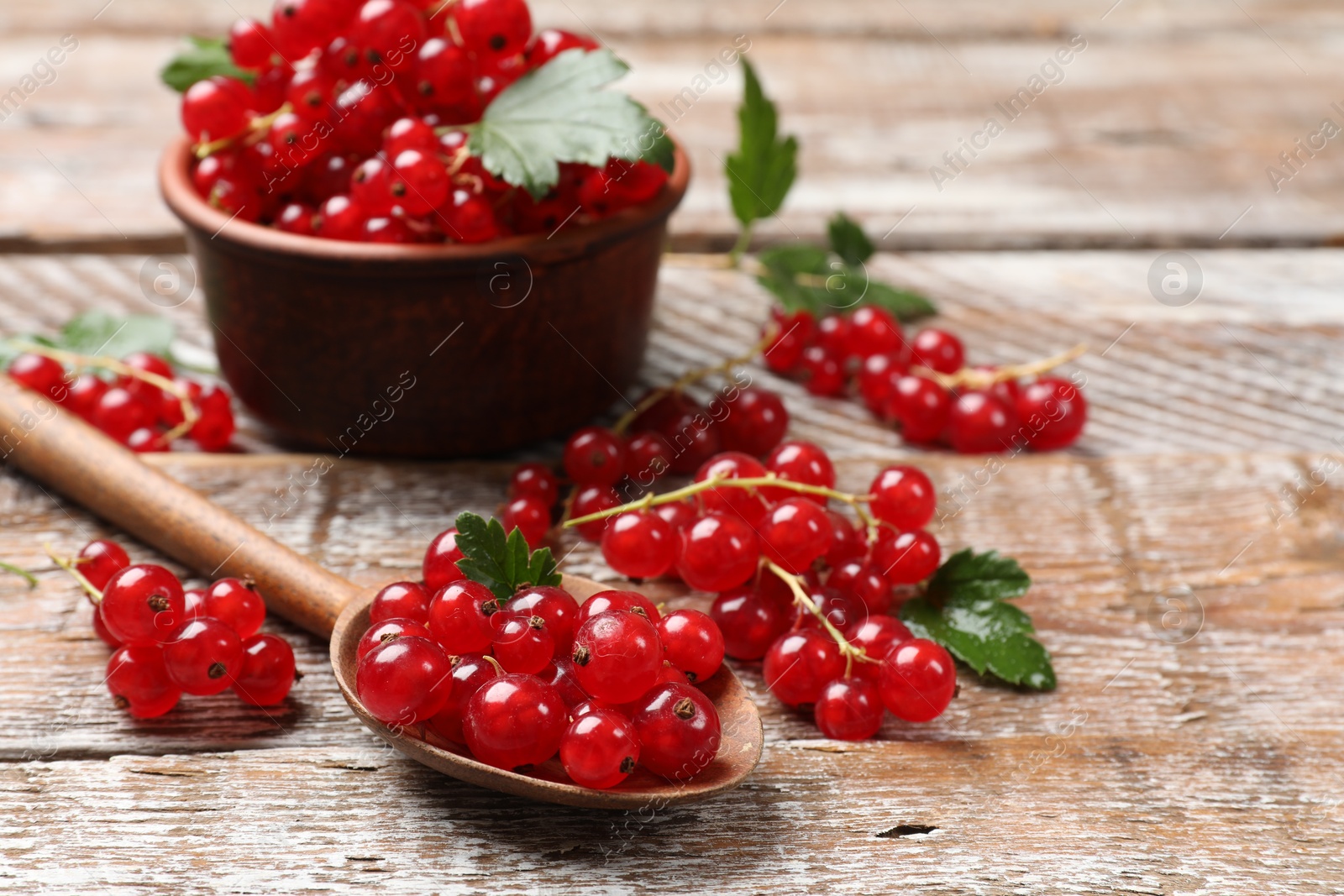 Photo of Fresh red currants and green leaves on wooden table, closeup