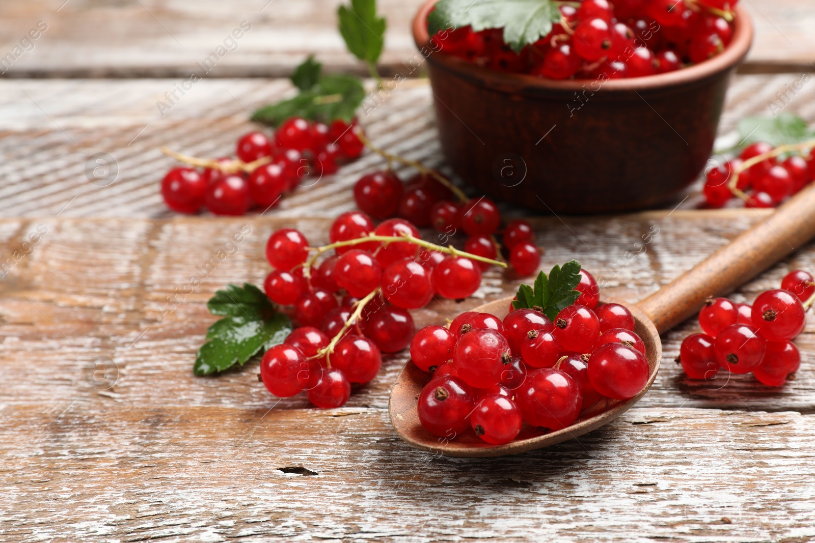 Photo of Fresh red currants and green leaves on wooden table, closeup