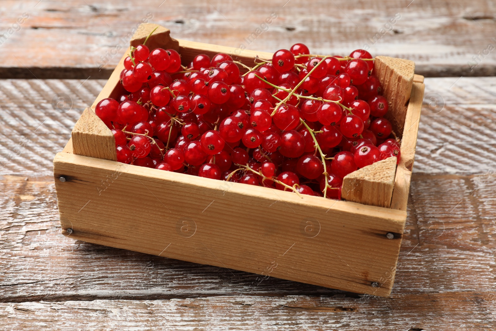 Photo of Fresh red currants in crate on wooden table, closeup