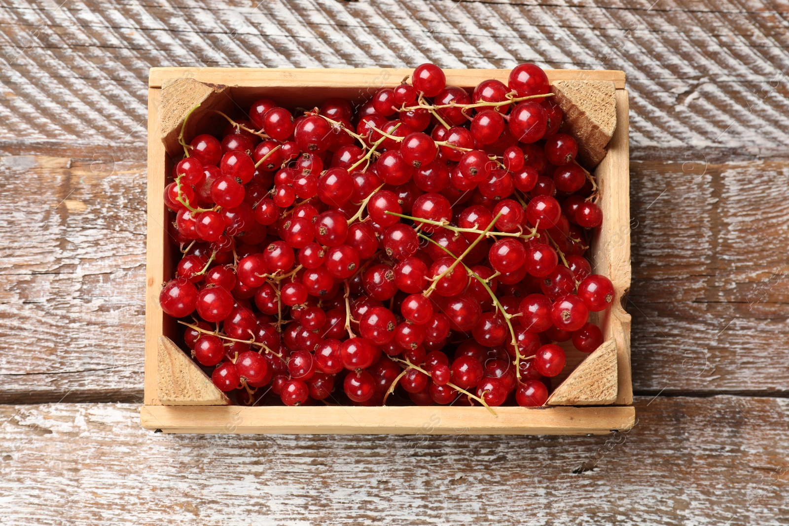 Photo of Fresh red currants in crate on wooden table, top view