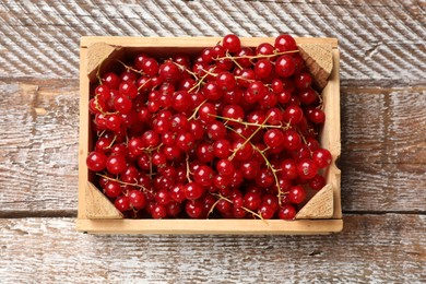 Fresh red currants in crate on wooden table, top view