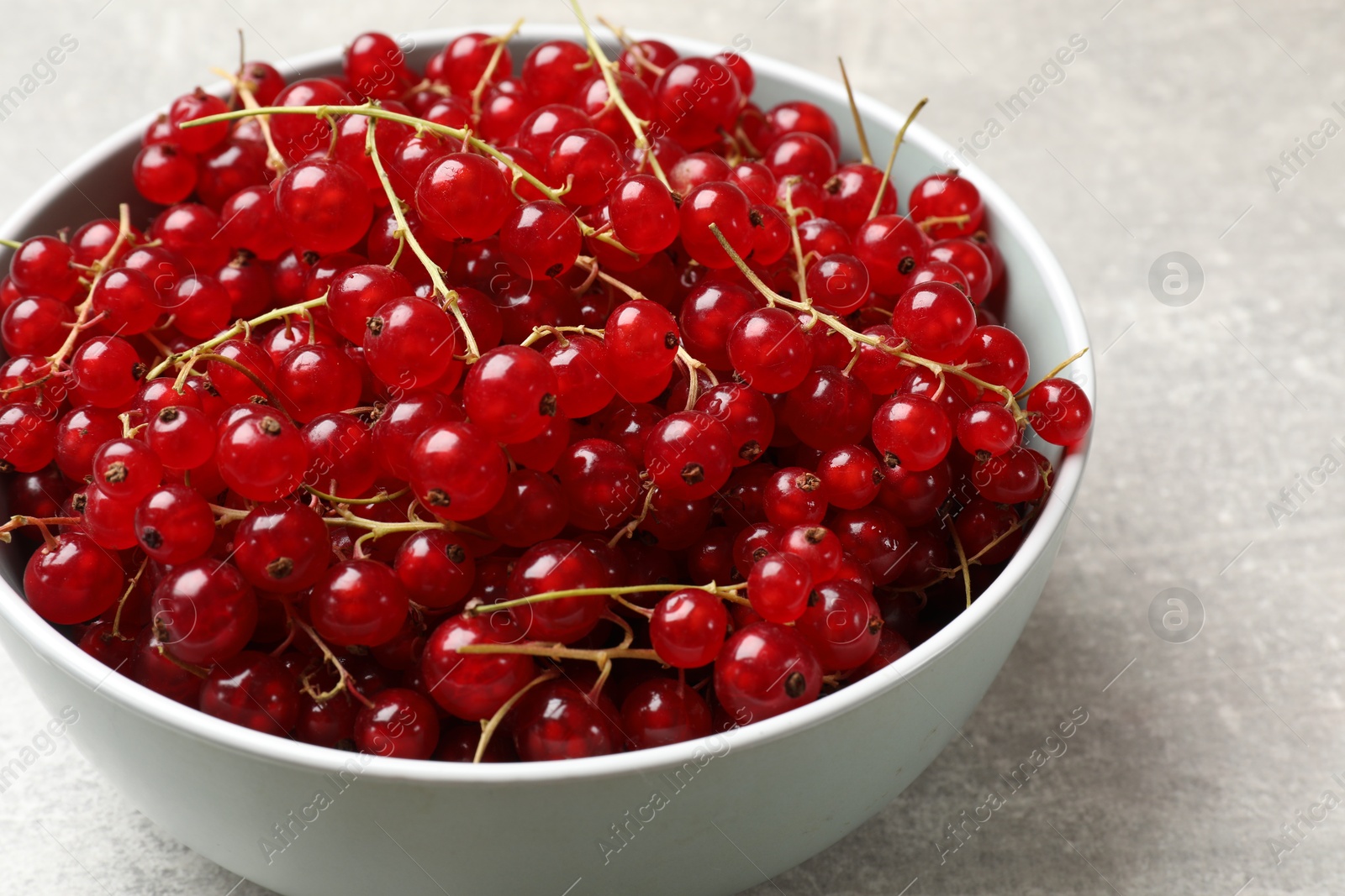 Photo of Fresh red currants in bowl on light grey table, closeup