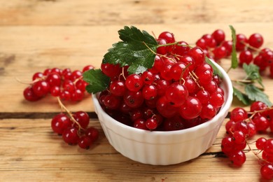 Photo of Fresh red currants and green leaves on wooden table, closeup