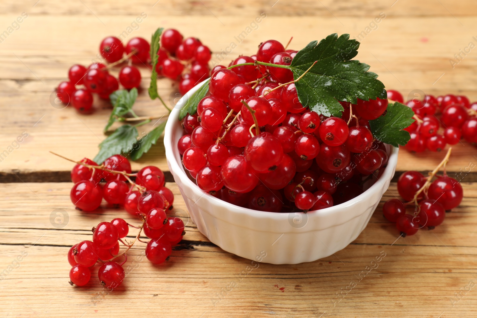 Photo of Fresh red currants and green leaves on wooden table, closeup