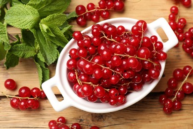 Photo of Fresh red currants in bowl and mint on wooden table, flat lay